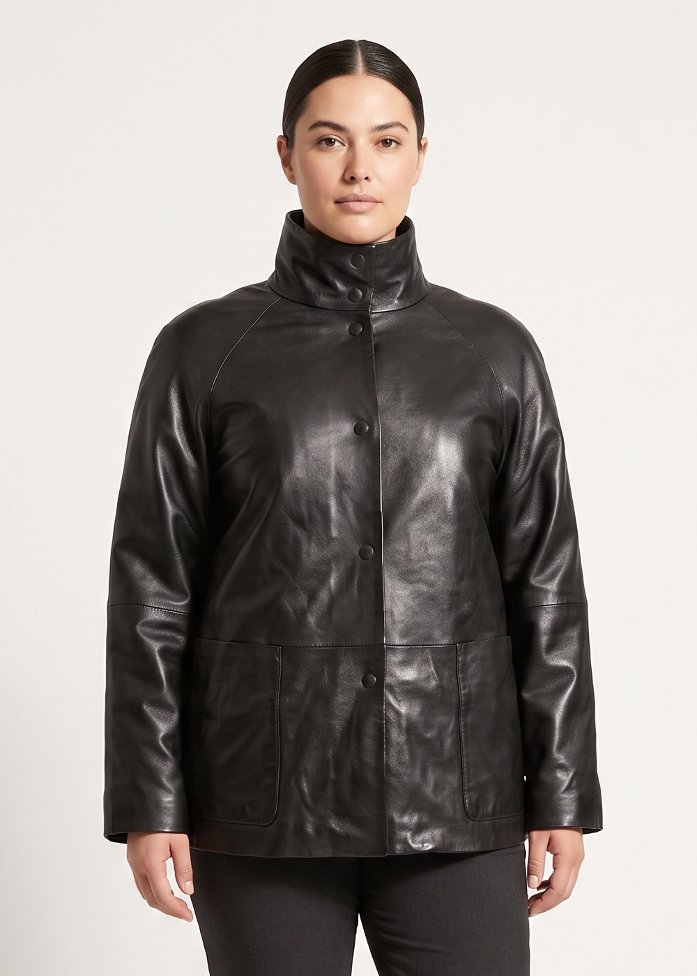 A model stands against a light gray studio background wearing a black leather jacket with a high collar, black trousers, and black boots.