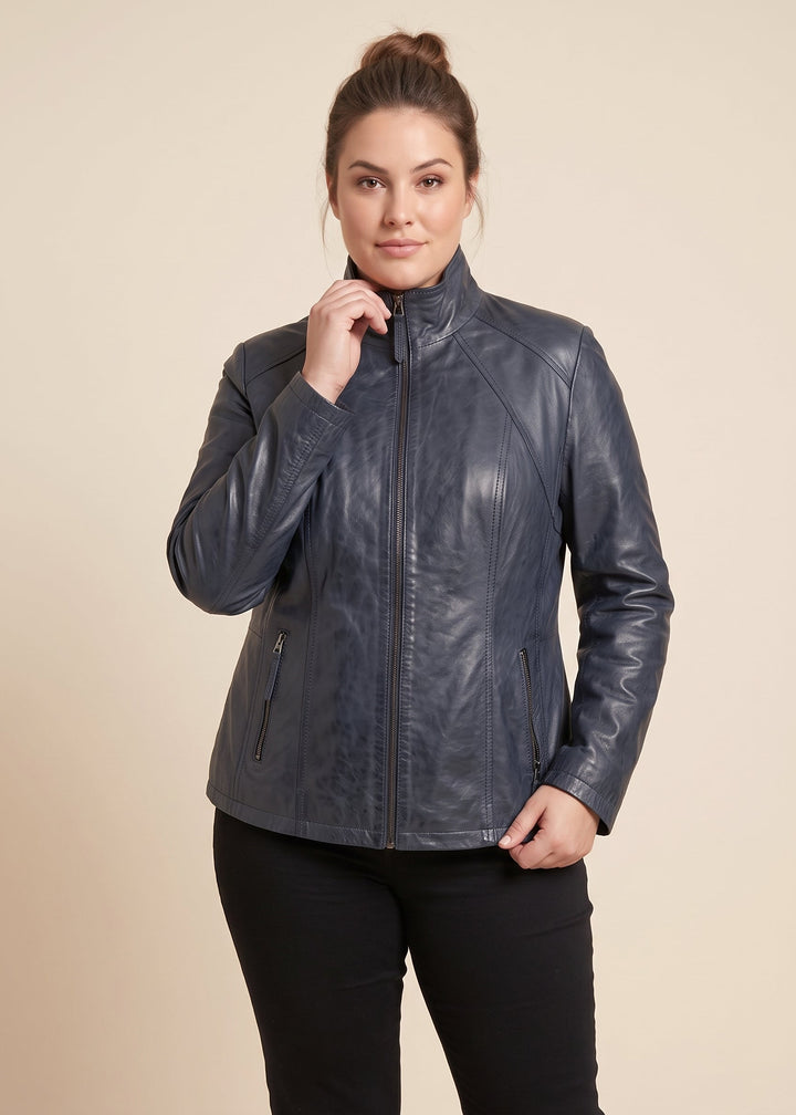 A woman modeling a dark slate blue real leather jacket with a high collar and front zipper, paired with black pants, against a solid beige background.