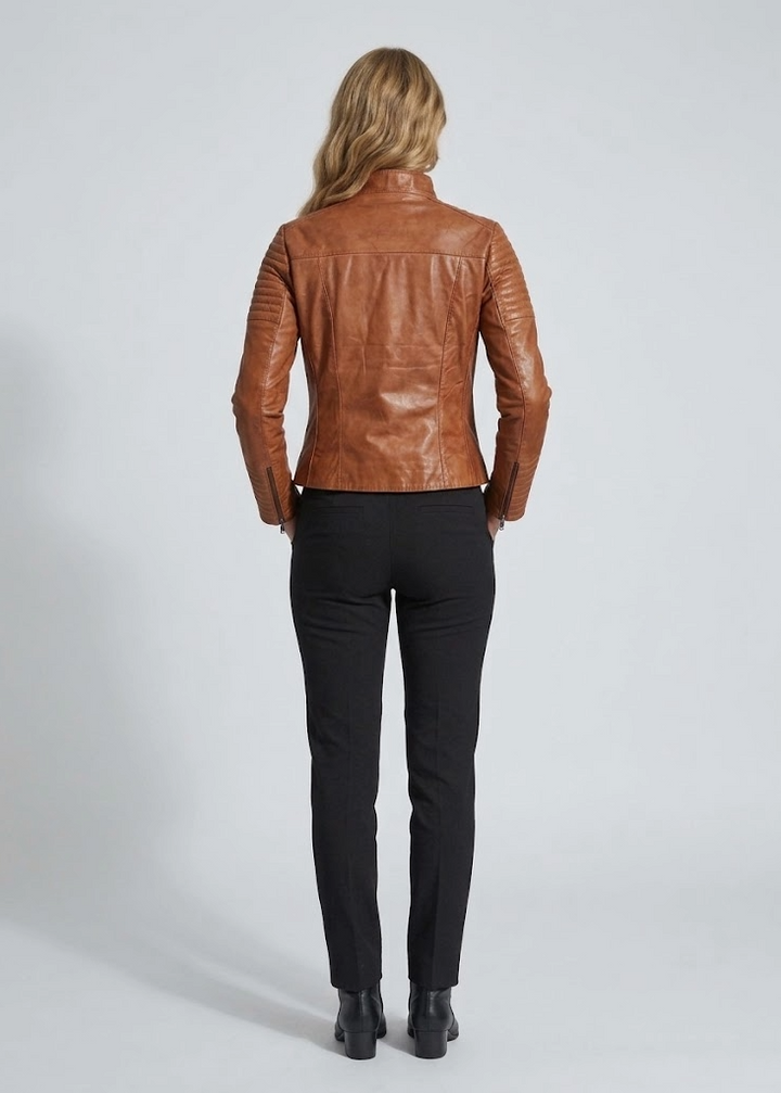 A woman viewed from behind wearing a fitted brown leather jacket, black trousers, and black ankle boots against a light gray studio background.